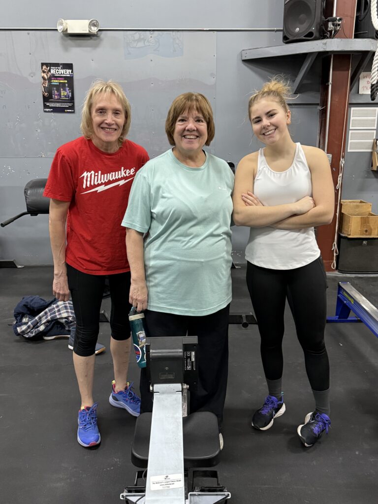 Three teammates smiling beside their rower